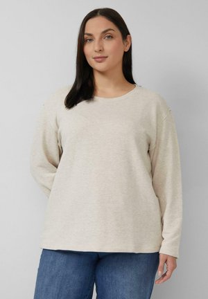 Felpa beige chiaro a maniche lunghe con scollo rotondo e vestibilità rilassata. Tessuto morbido, dettagli di cuciture minime, indossata con jeans blu.