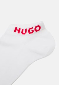 Fehér pamut zokni bordás textúrával, piros "HUGO" logóval a szélén. Kényelmes és hétköznapi viseletre tervezték.