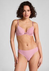 Helles rosa BH mit vorgeformten Cups und dünnen verstellbaren Trägern, mit einem dekorativen Detail zwischen den Cups. Passende hellrosa Bikiniunterhose.