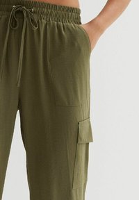 Oliwkowe spodnieCargo z elastycznym paskiem, teksturowana tkanina, boczne kieszenie oraz kieszeń naszywana na udzie.
