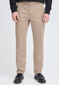 Chino beige in cotone con vestibilità dritta. Presentano una chiusura con bottone, passanti per la cintura e tasche laterali. Indossati con mocassini neri.