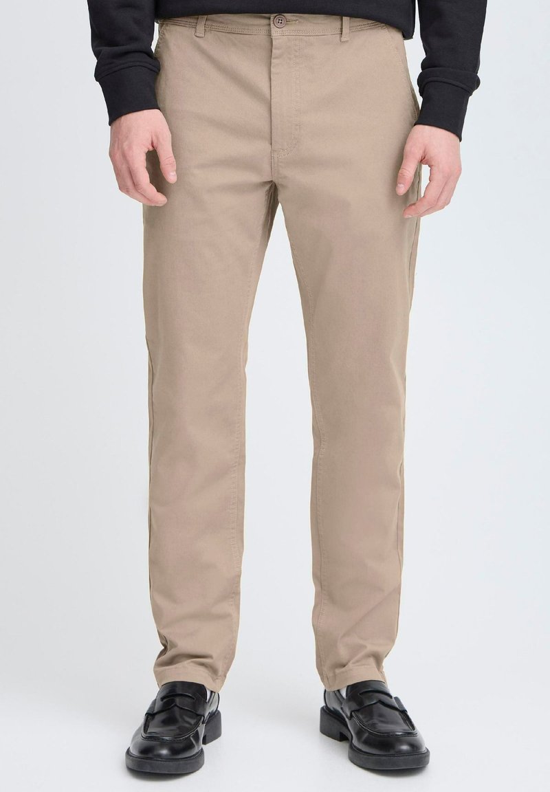 Chino beige in cotone con vestibilità dritta. Presentano una chiusura con bottone, passanti per la cintura e tasche laterali. Indossati con mocassini neri.