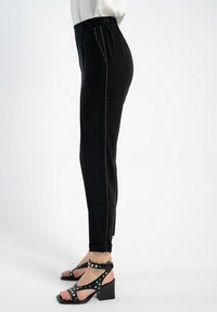 Czarne spodnie z elastycznym pasem, o dopasowanym kroju, z kontrastującymi białymi przeszyciami po bokach, zestawione z czarnymi sandałami na obcasie.