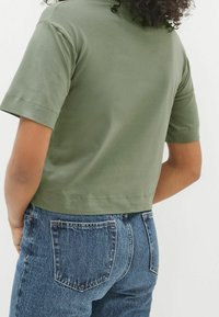 Oliwkowy, skrócony t-shirt z krótkim rękawem, wykonany z miękkiej bawełny. Połączony z niebieskimi dżinsami z wysokim stanem, posiadającymi tylne kieszenie.