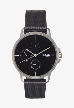 Schwarze Hugo Boss Armbanduhr mit silbernem Gehäuse, schwarzem strukturiertem Armband, drei Hilfszifferblättern für 24-Stunden, Datum und Wochentag sowie silbernen Stundenmarkierungen.