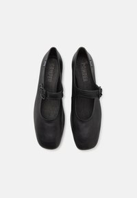Paire de chaussures Mary Jane en cuir noir avec bouts carrés et brides à boucle réglables, vues de dessus sur fond blanc.