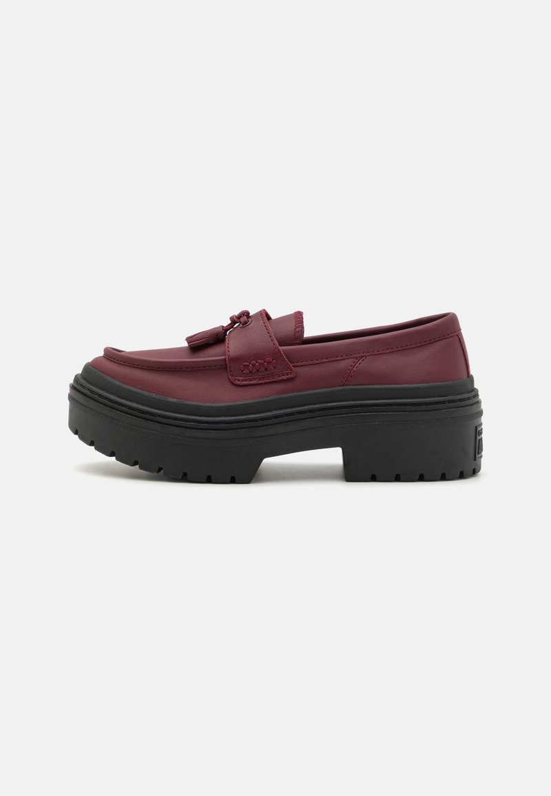 Burgundy synthetic loafers with a flat black rubber platform sole, featuring a raised seam, decorative tassels, and a sleek design.