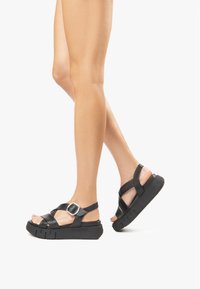 Black leather strappy sandals with a chunky sole and a silver buckle accent, featuring an open toe design and textured rubber outsole.