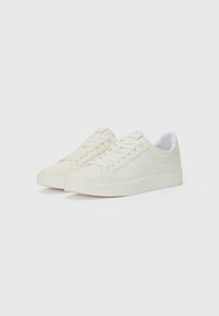 White canvas sneakers with a low-top design, textured surface, flat laces, and a reinforced heel. Subtle side accents in the same color.
