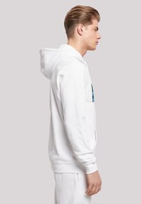 Balts kapučinīgs džemperis ar kangaroo kabatu un regulējamu auklu kapuci. Gluda kokvilnas materiāla, brīva piegriezuma un minimālisma dizaina.