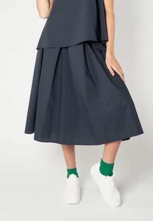 Gonna plissettata blu scuro realizzata in tessuto leggero, abbinata a sneakers bianche e calzini verdi a costine. Il design presenta una silhouette fluida.