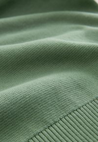 Țesătură din amestec de bumbac, de culoare verde salvie moale, cu o textură netedă, având detalii cu nervuri pe margine și modele subtile de țesătură.