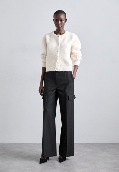 Cardigan in maglia crema con scollo rotondo e chiusura a bottoni, abbinato a pantaloni cargo neri a vita alta con tasche laterali.