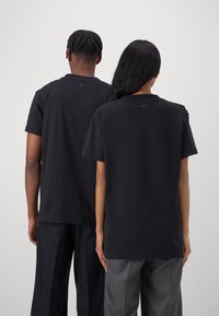 Camisetas de algodón negras de manga corta, de corte relajado, con cuello redondo y un sutil detalle de logo cerca del cuello.
