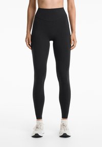 Leggings noirs taille haute en tissu extensible, présentant une texture lisse et une silhouette ajustée, associés à des baskets légères.
