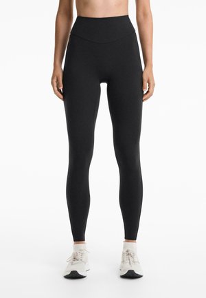 Hochbundige schwarze Leggings aus dehnbarem Stoff, mit einer glatten Textur und einer figurschmeichelnden Silhouette, kombiniert mit leichten Sneakers.