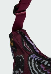 Maroon fabric bag featuring floral patterns, zip closure with purple pull tab, and adjustable strap. Textured exterior with contrasting designs.