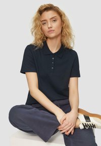Marineblauwe polo met een kraag en vier knopen, gemaakt van zachte stof. Gecombineerd met losse marineblauwe broek en witte sneakers met zwarte accenten.