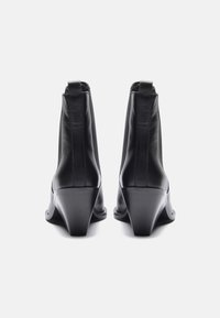 Botines de cuero negro con tacón afilado, textura suave y paneles laterales elásticos, que presentan un diseño minimalista sin herrajes visibles.