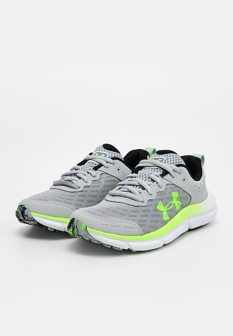 Par de zapatillas de running de malla gris con acentos en verde neón, forro interior negro, suelas blancas y logotipo de Under Armour en el lateral.