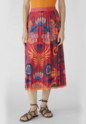 Jupe midi plissée en rouge vif avec des motifs floraux et tropicaux en bleu et orange. Taille élastique avec un détail texte "TROPICAL".