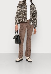 Leopardmönstrad jacka, vit ribbad polotröja, bruna byxor med paisleymönster, svart handväska med strukturerat handtag, krämfärgade snörboots med svarta sulor.