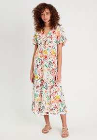 Robe midi florale en tissu léger blanc, ornée d'impressions colorées de fleurs et de visages. Manches courtes volantées et un détail à nouer sur le devant.