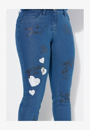 Modré džíny z denimu s různými potisky, včetně černého textu a bílých srdcí, spolu s grafikou kolečkových bruslí.