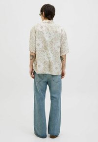 Camisa de botones de manga corta con un patrón floral en tonos suaves de beige y verde, combinada con unos pantalones vaqueros de pierna ancha en azul claro.