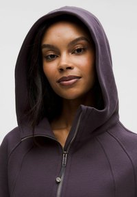 Kapuzenpullover aus tiefviolettem Stoff mit gerippter Struktur. Verfügt über einen durchgehenden Reißverschluss und verstärkte Nähte, die das moderne Sportdesign betonen.