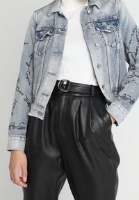 Ljust blå denimjacka med urtvättad finish, prydd med svarta handskrivna detaljer, kombinerad med höga svarta läderbyxor och en vit topp.