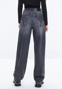 Vaqueros de pierna ancha de tiro alto en negro con un acabado desgastado, que cuentan con dos bolsillos traseros y un diseño de corte recto. El material es denim.