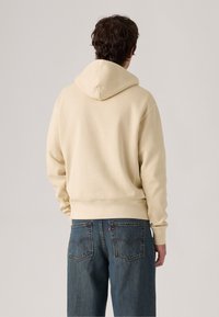 Beige hoodie met een trekkoordkap, textuurstof, en een geribbelde onderrand, gecombineerd met blauwe denim jeans met achterzakken.