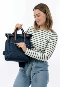 Tumed sinine seljakott pruunide nahkaelementidega, lukuga taskud ja struktureeritud disain. Valmistatud vastupidavast kangast, omab kaht käepidet ja rihma.