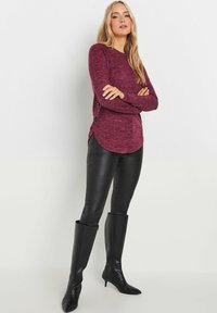 Bordeaux lange mouwen top met een gemêleerde textuur en zijknoppen, gecombineerd met zwarte leren leggings en kniehoge puntige laarzen.