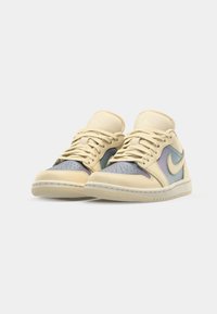 Beige Nike sportcipők kék irizálópanellel és perforált orral. A fűzők meg vannak kötve, a design oldalán pedig a Nike logó található.