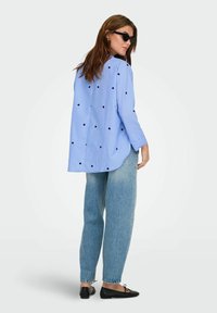 Mėlynos dryžuotos ilgomis rankovėmis marškiniai su juodais širdelių raštais, kreivo kirpimo apatinė briauna, dėvimi su šviesiai mėlynomis plačiomis kelnėmis ir juodomis butais. Akiniai nuo saulės papildo šį įvaizdį.