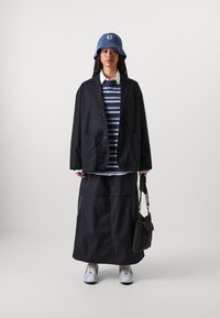 Svart jakke, blåstripete genser, lang svart skjørt, blå bøttehatt, hvit skjorte under, grå joggesko, svart veske med stropper.