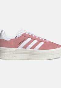 Zapatilla Adidas Gazelle rosa con rayas blancas, suela gruesa color crema, cordones blancos y logo de Adidas embosado en el lateral de la suela.
