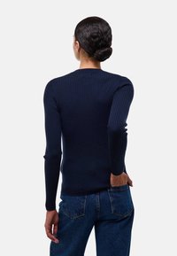 Pull-over en maille côtelée bleu marine à manches longues avec un col rond, au design ajusté et en tissu texturé, associé à un jean en denim bleu taille haute.