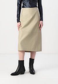 Khaki midi-skjørt i en strukturert stoff med sidelommer, kombinert med svarte høye ankelstøvler. Toppen har en mørk satengfinish.