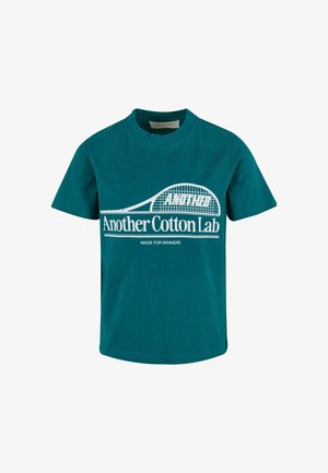 Camiseta de algodón en color verde azulado con mangas cortas, escote redondo y texto en blanco. Presenta un diseño de raqueta de tenis y la frase "Hecha para ganadores".