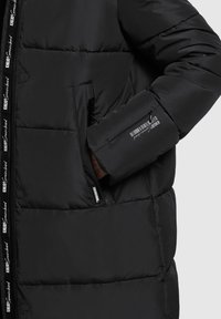 Schwarze Daunenjacke mit gestepptem Design, Reißverschlusstaschen und Branding auf dem Reißverschlussband. Bietet eine bequeme Passform und eine glatte Textur.