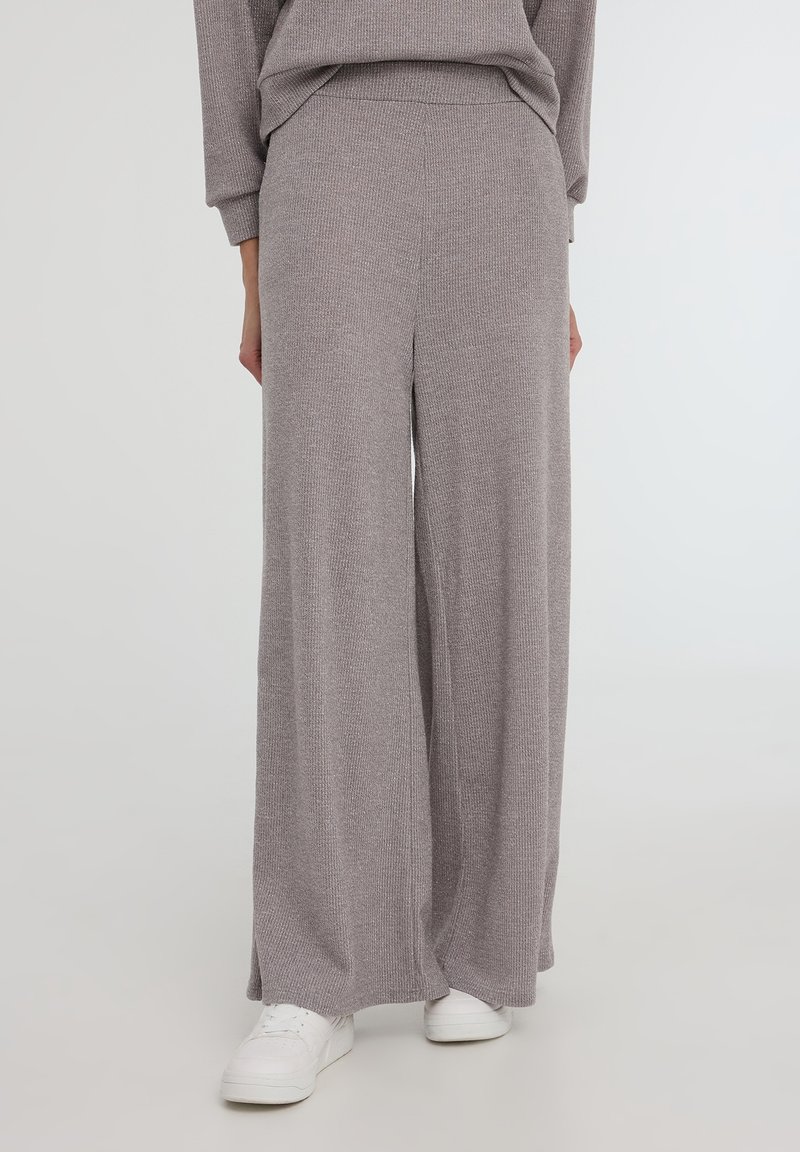 Pantaloni grigi a gamba larga realizzati in tessuto di maglia a costine, con cintura elastica e texture morbida, abbinati a sneakers bianche.