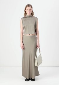Ärmelloses, hochgeschlossenes Crop-Top und bodenlanger Rock aus weichem, gedämpften olivgrünem Stoff. Kombiniert mit einer hellgrauen Umhängetasche und schwarzen Schuhen.