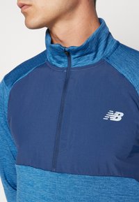 Maglia sportiva mezza zip blu e navy con un tessuto testurizzato, caratterizzata da un logo sul petto e dettagli a contrasto sulle spalle.