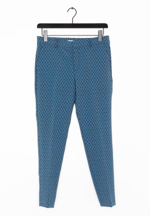 Niebieskie spodnie w wzory z geometrycznym motywem, z elastycznym pasem i gładkiego materiału. Wiszą na czarnym plastikowym haczyku.