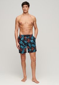 Shorts da bagno da uomo con base nera, caratterizzati da un vivace motivo tropicale di foglie blu e rosse, vita elastica e tasche laterali.