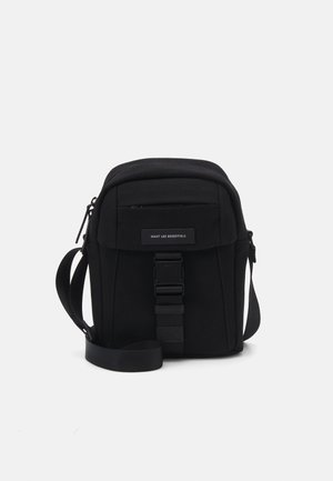 Čierna látková crossbody taška s obdĺžnikovým tvarom, zipsovým uzatvorením, nastaviteľným popruhom a predným prackovým detailom. Minimalistický dizajn.