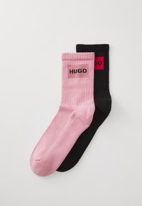 Pair of ribbed socks, one pink and one black, each with a rectangular logo patch featuring the word "HUGO" near the top cuff.